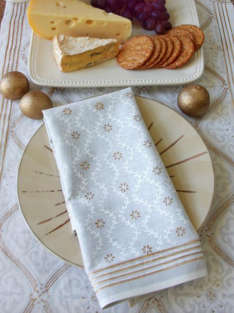 white and gold cloth napkins upon a white and gold tablelcloth with cheese and crackers at the side