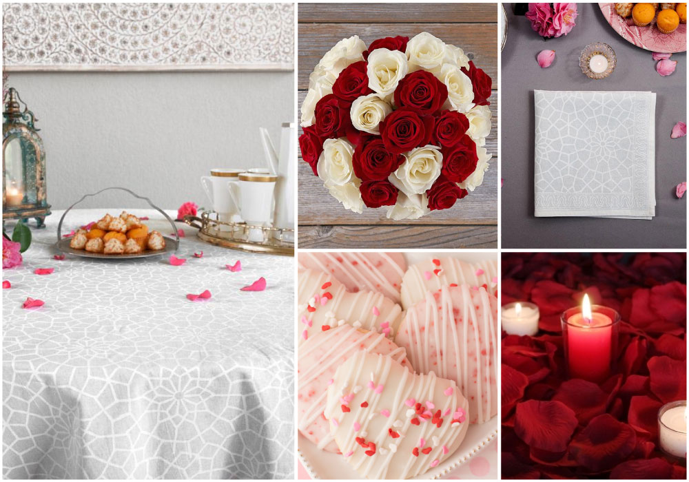 A white tablecloth styled for Valentine's Day table setting with red roses, flower petals, candles, and heart-shaped tea cakes