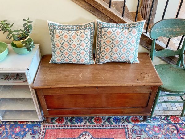 two throw pillows in an Indian print on an entry bench surrounded by eclectic decor