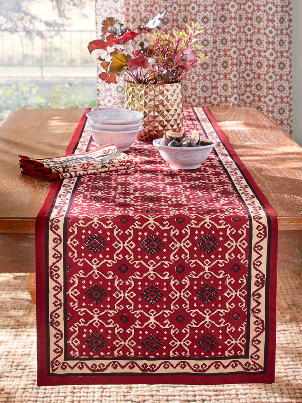 A festive table runner, Ruby Kilim, with black and cream accents on a medium-brown table with a metal centerpiece vase