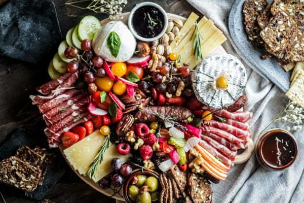 Photograph of a charcuterie board filled with cured meats, cheeses, fruits, olives, and crackers on a linen table cloth