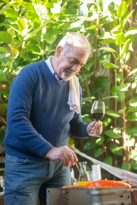Photograph of man grilling outside with a wine glass in hand