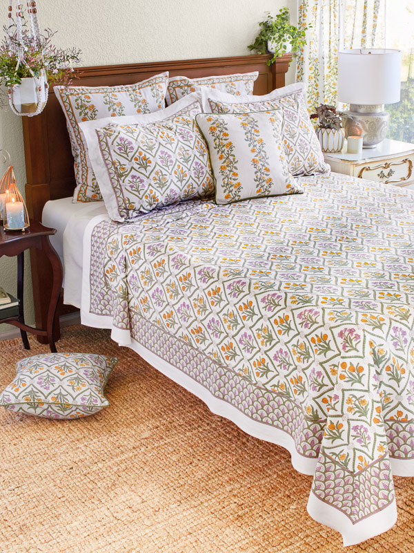 Photograph of a bedroom featuring a bed covered in a lightweight summer bedspread with a floral print of irises, tulips, and daffodils
