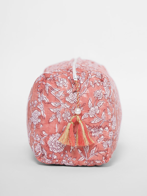Photograph of a cosmetics bag featuring white flowers on a coral pink background, emphasing the luxurious touch of a handmade tassel