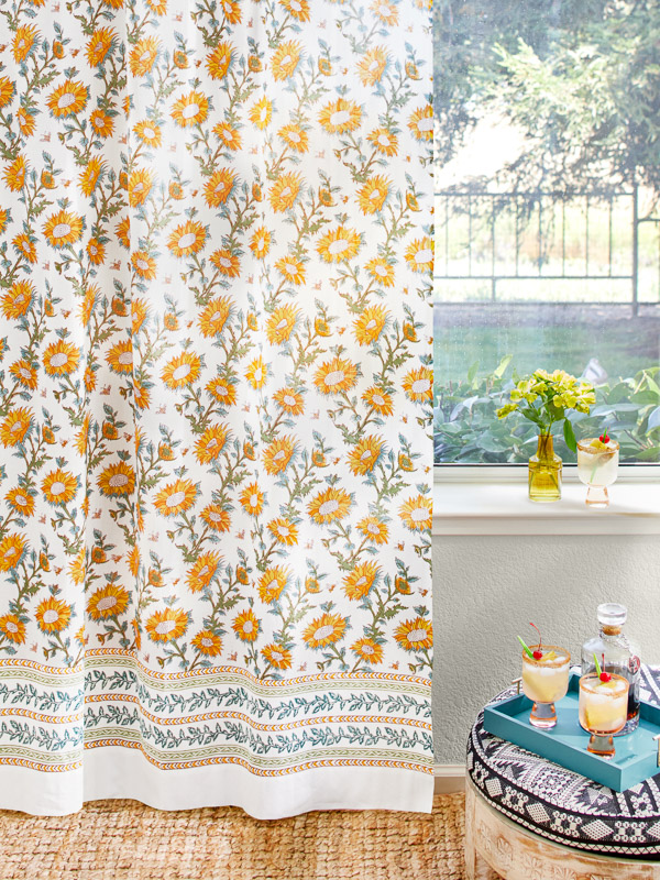 Photograph of a sunflower print curtain featuring yellow, orange, and green sunflowers on a ground of white